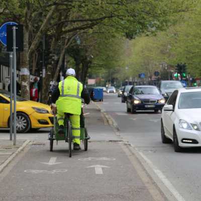 Radfahrer in Warnkleidung fährt neben Autos durch eine belebte Straße in Tirana, Albanien.
