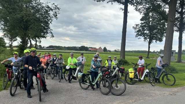 Eine Gruppe von Menschen mit Fahrrädern und Helmen steht auf einer asphaltierten Straße.