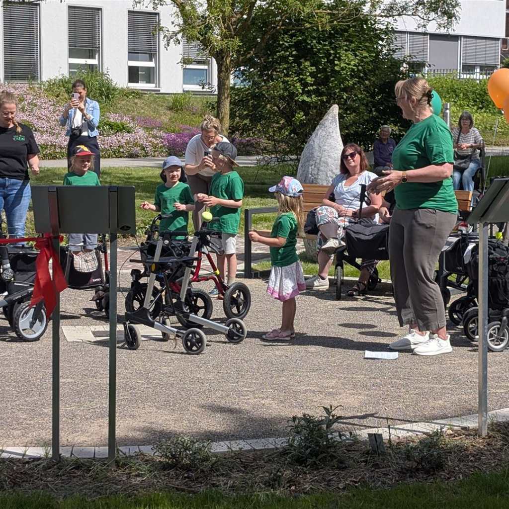 Kinder und Erwachsene im Freien, einige mit Gehhilfen, bunte Ballons schweben